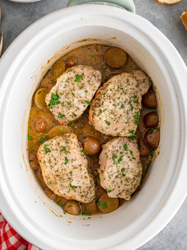 Four pork chops with baby potatoes in a crockpot.