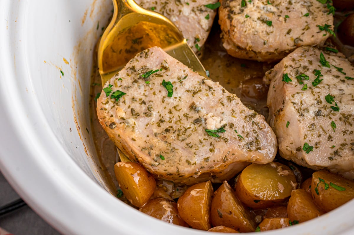 A gold spatula grabbing a pork chop from a slow cooker.