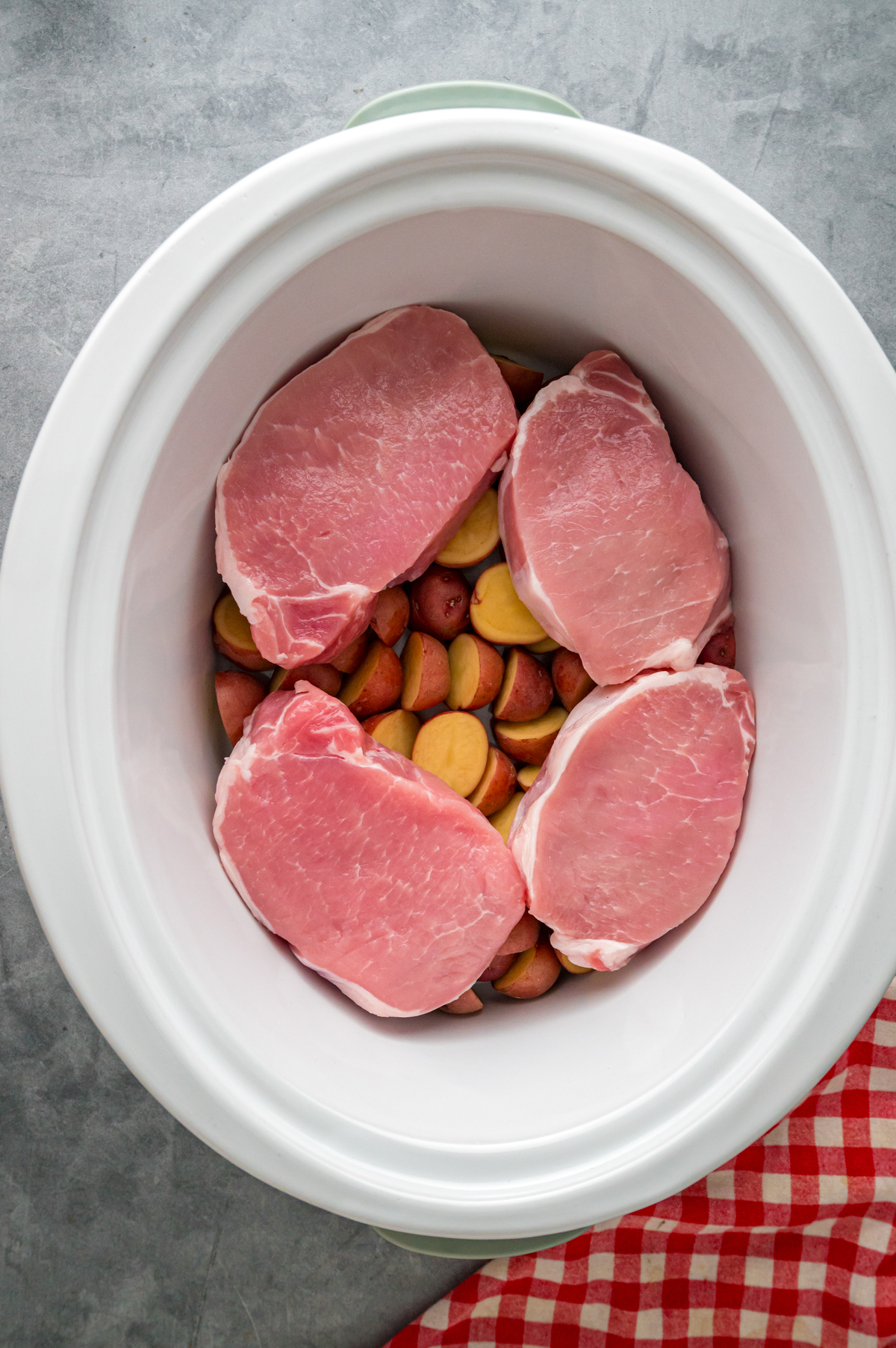 Raw potatoes and pork chops in a slow cooker.
