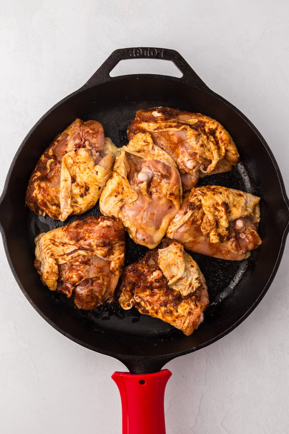seasoned chicken thighs in a skillet browing.