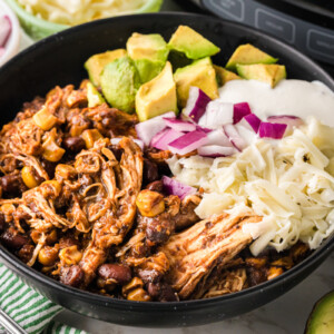Close-up of a bowl with shredded chicken, beans, and corn and toppings.