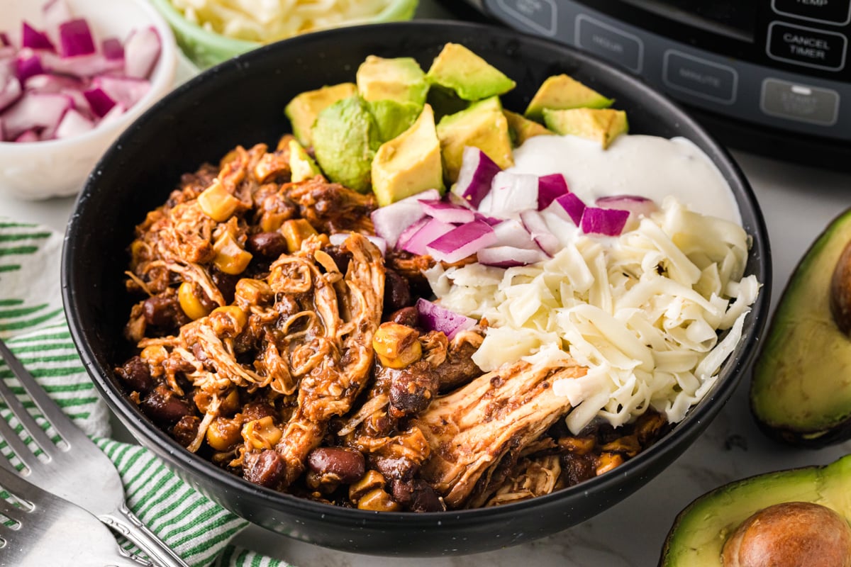 Close-up of a bowl with shredded chicken, beans, and corn and toppings.