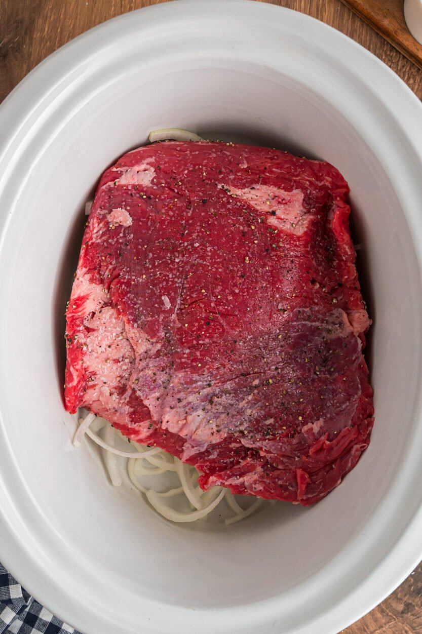 Seasoned flank steak over garlic and onion in a slow cooker.