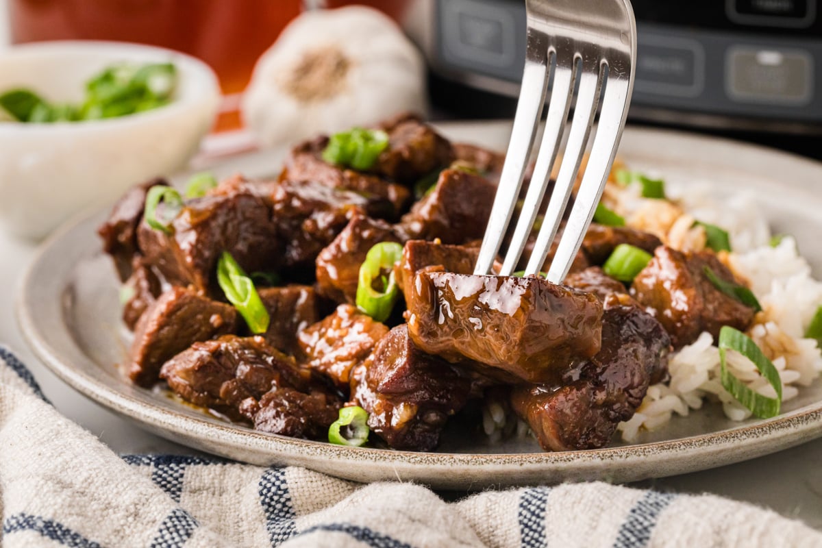 A fork grabbing a bite of steak from a plate.