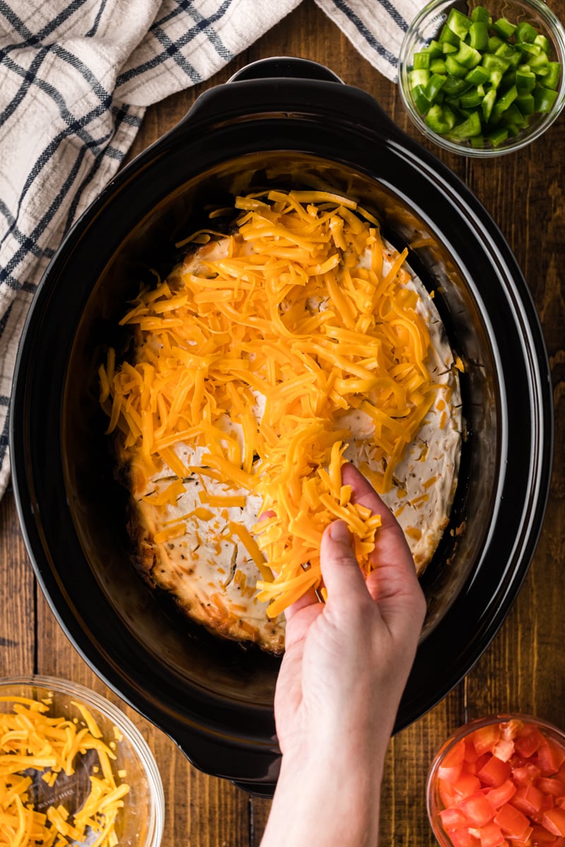 Sprinkling cheddar cheese on top of ingredients in a crockpot.