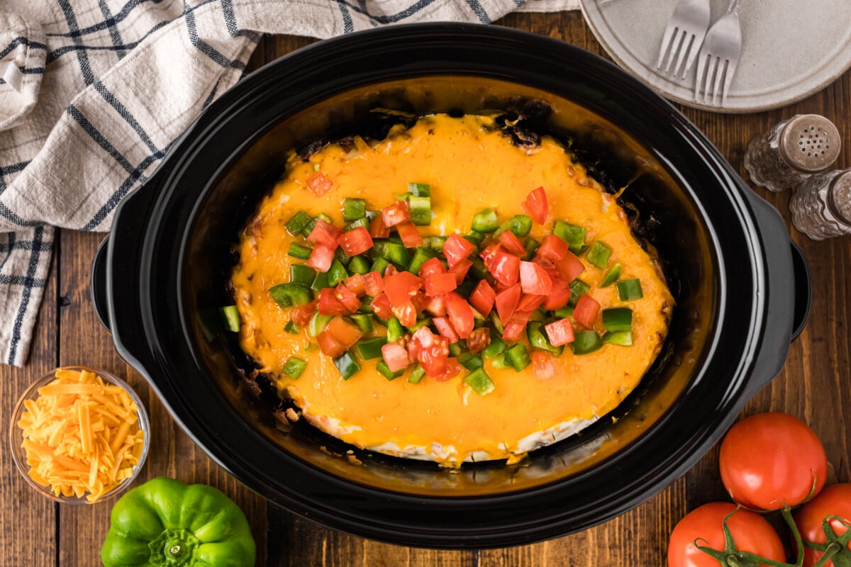 John Wayne casserole in a crockpot with bell pepper and tomato on top.