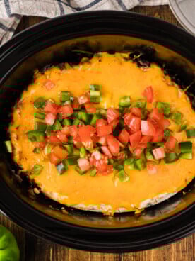 John Wayne casserole in a crockpot with bell pepper and tomato on top.