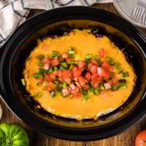 John Wayne casserole in a crockpot with bell pepper and tomato on top.