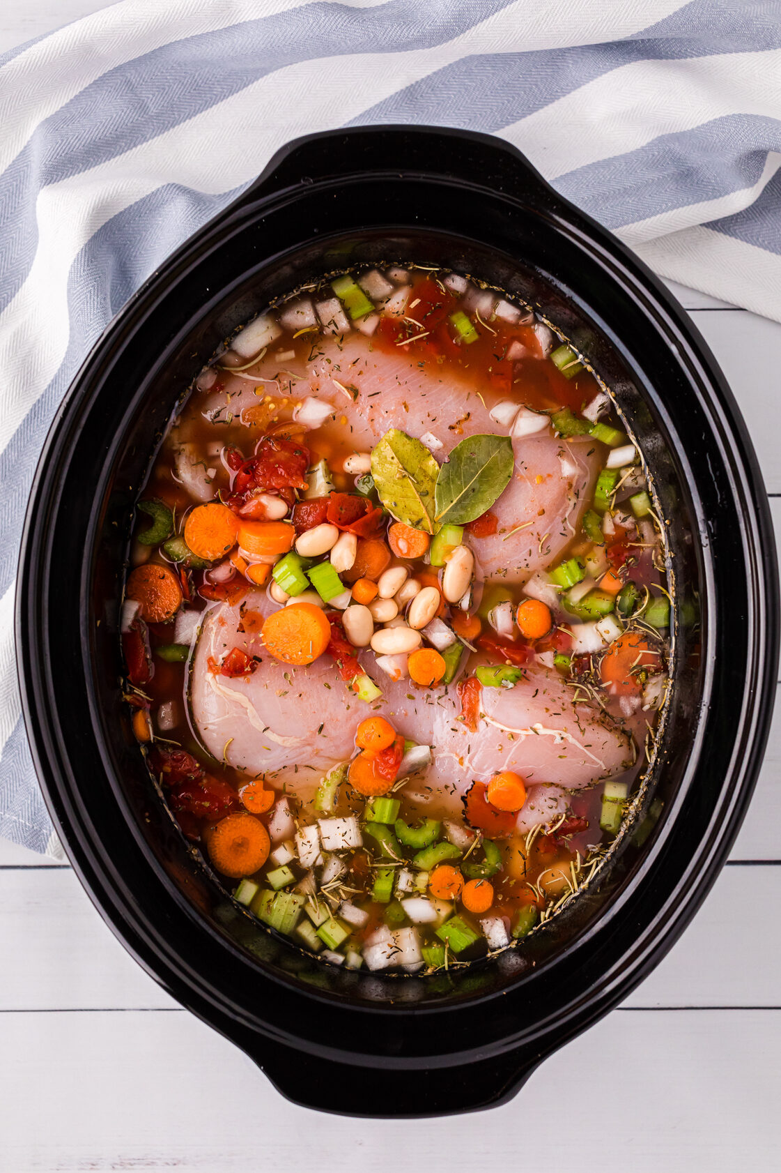 Vegetables, beans, chicke and broth in a slow cooker.