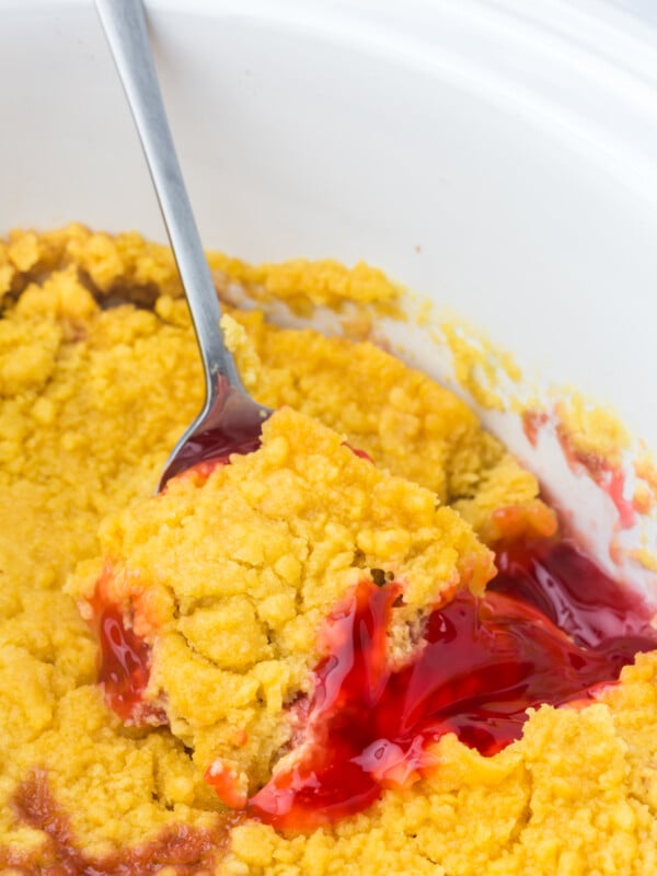 A spoon scooping Strawberry Rhubarb Dump Cake from a crockpot.