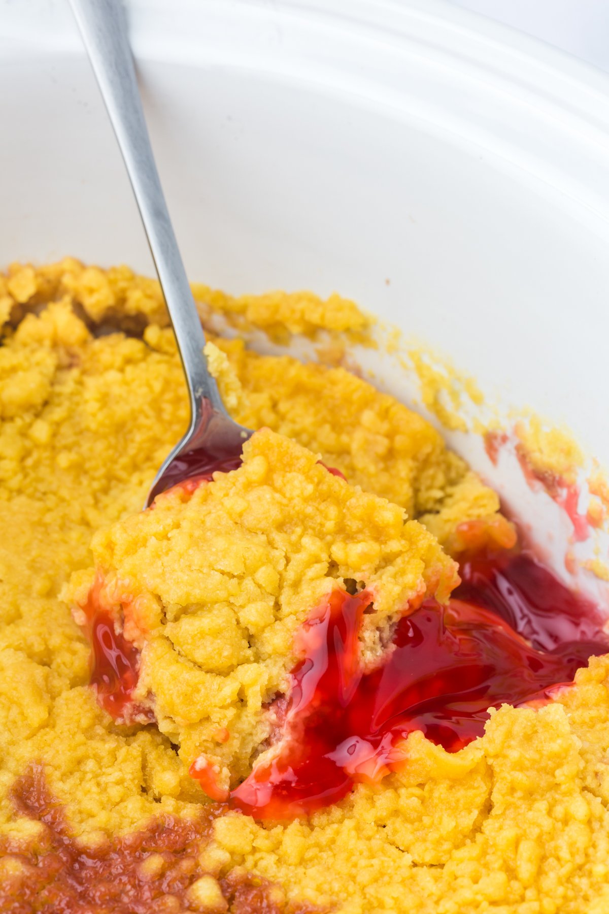 A spoon scooping Strawberry Rhubarb Dump Cake from a crockpot.