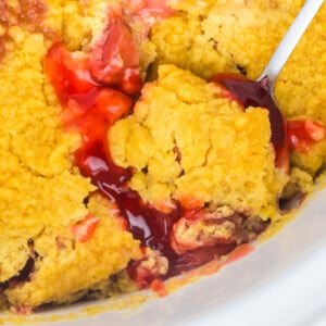 A scoop of dump cake on a spoon about to be taken out of a crockpot.