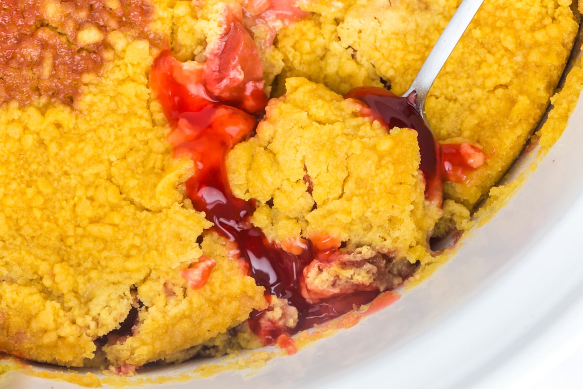 A scoop of dump cake on a spoon about to be taken out of a crockpot.