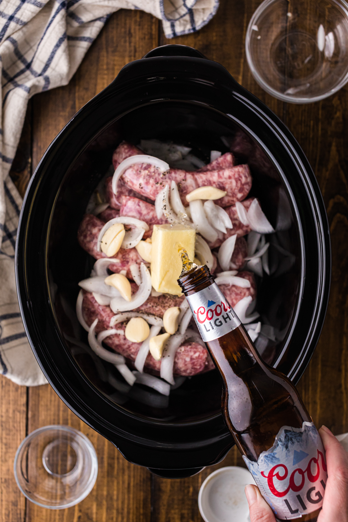 Pouring beer into a crockpot over brats.