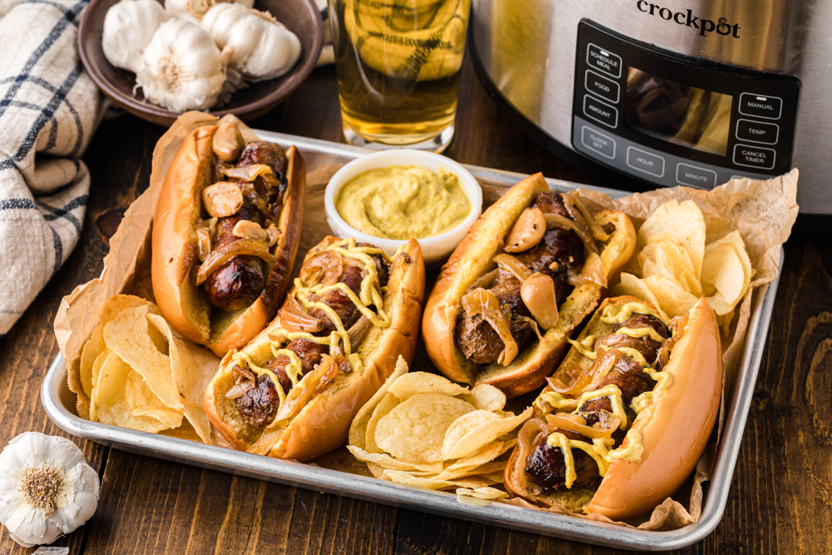 Brats in buns on a baking sheet, some with mustard.
