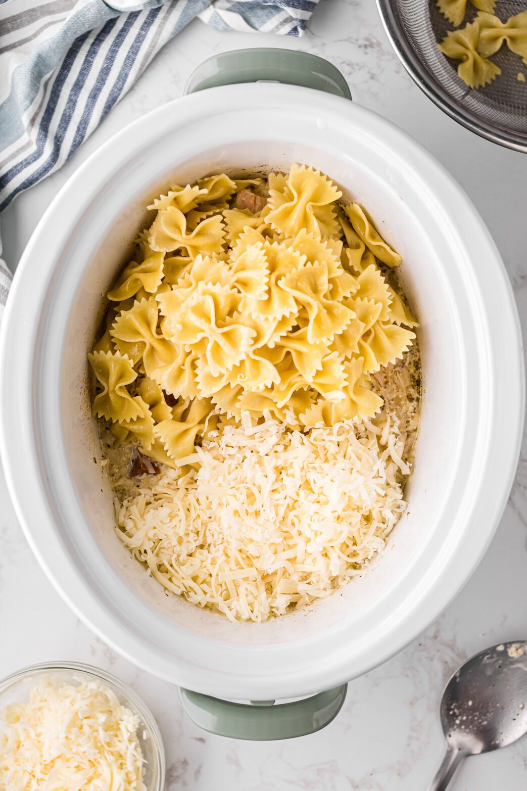 Pasta and cheese added to shredded chicken mixture in a crockpot.