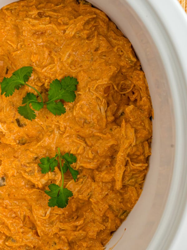 Creamy salsa chicken in a crockpot with cilantro garnish.