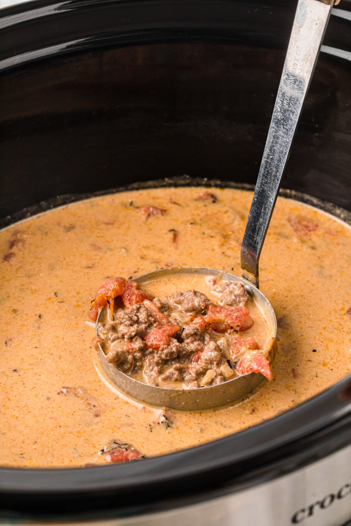 A ladleful of creamy taco soup in a crockpot.