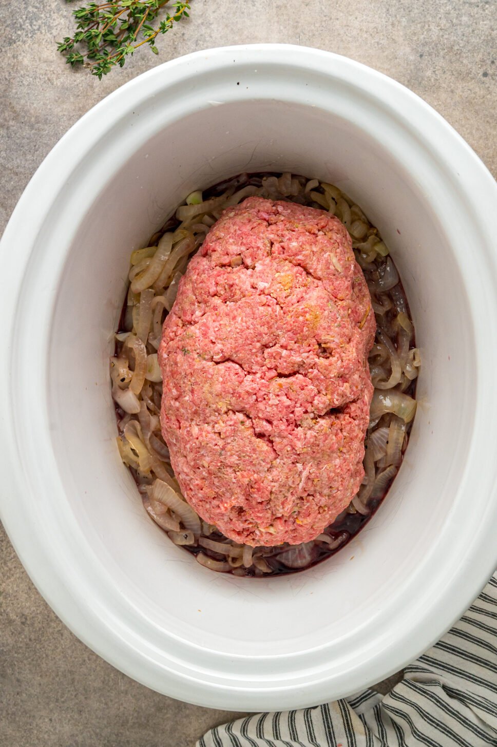 Formed meatloaf on top of onions in a slow cooker.