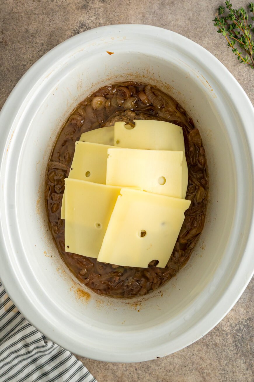 Slices of Swiss cheese on top of meatloaf in a slow cooker.