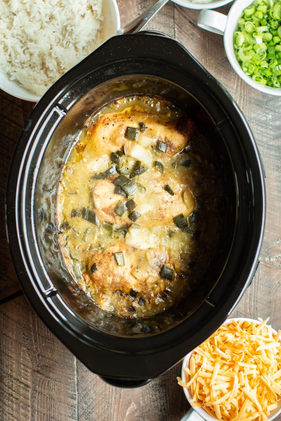 cooked chicken breasts with green chiles, onion and green enchilada sauce in a slow cooker.