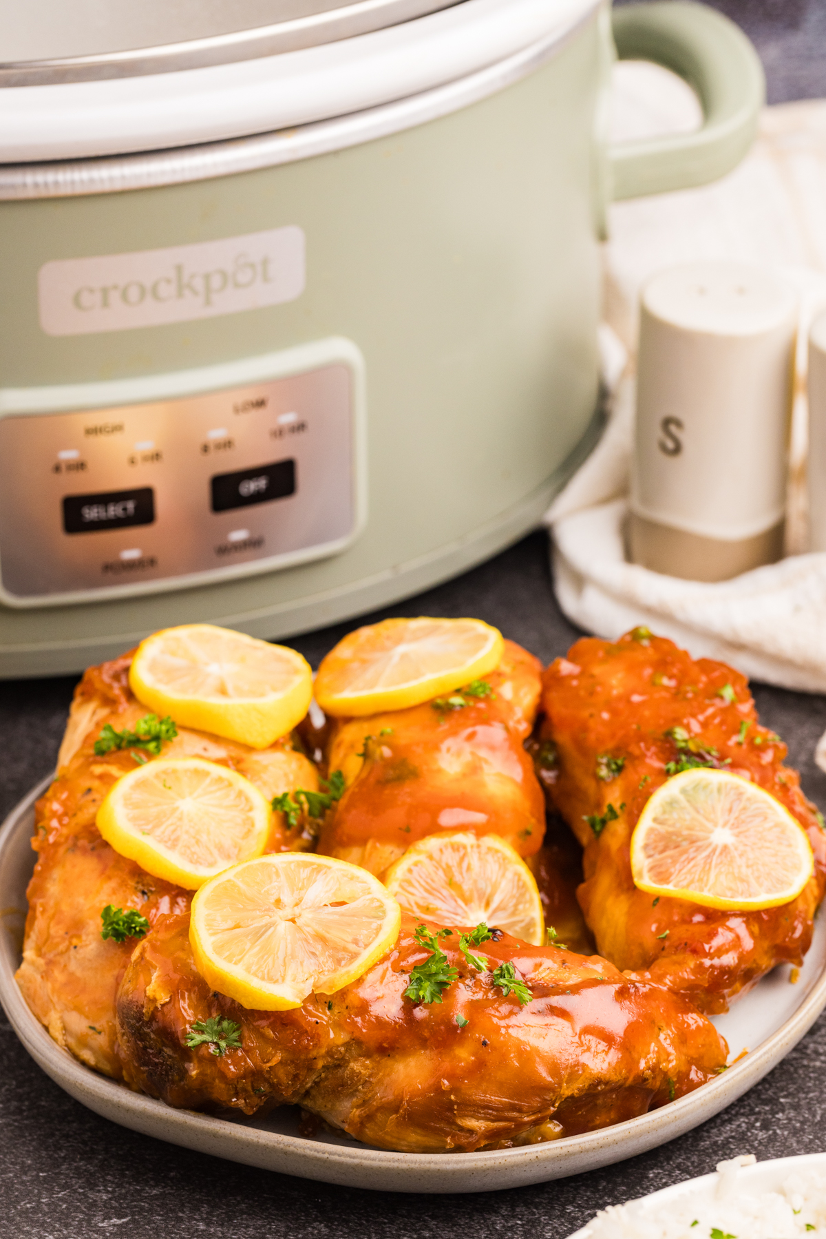 A plate of lemonade chicken in front of a slow cooker.