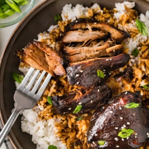 Shredded yoshida's chicken and rice on a plate with a fork taking a bite.