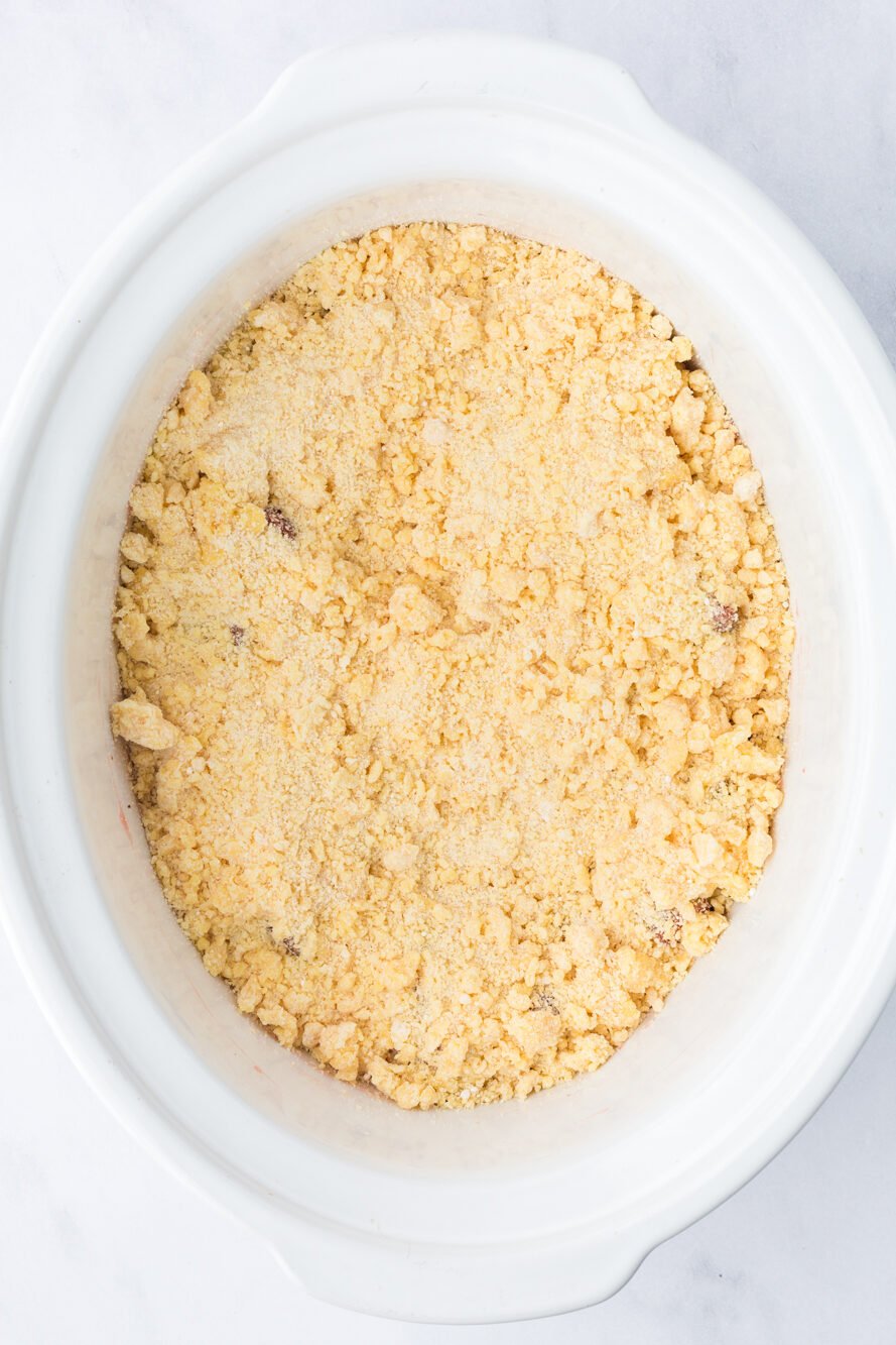 Cake mix and butter crumble mixture on top of rhubarb and strawberry jelly in a crockpot.
