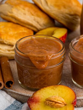 Two jars of peach butter on a tray with biscuits.