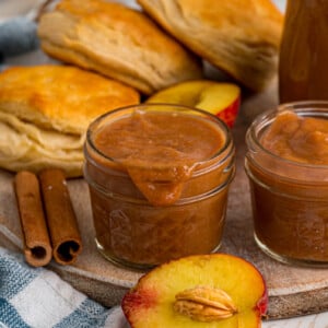 Two jars of peach butter on a tray with biscuits.