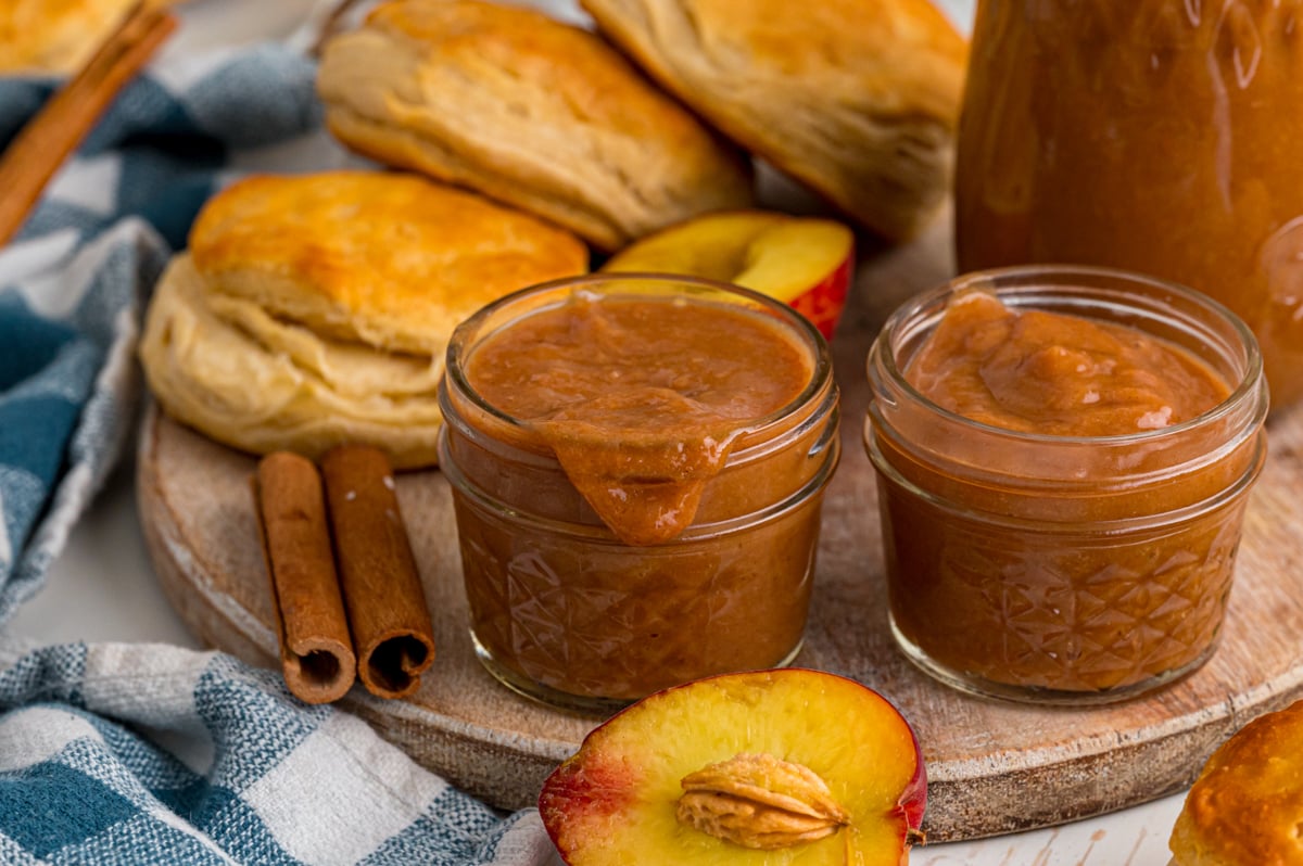 Two jars of peach butter on a tray with biscuits.
