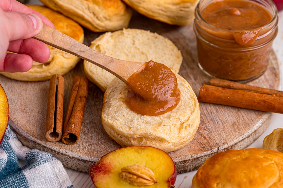 Spreading peach butter onto a biscuit with a small wooden spoon.