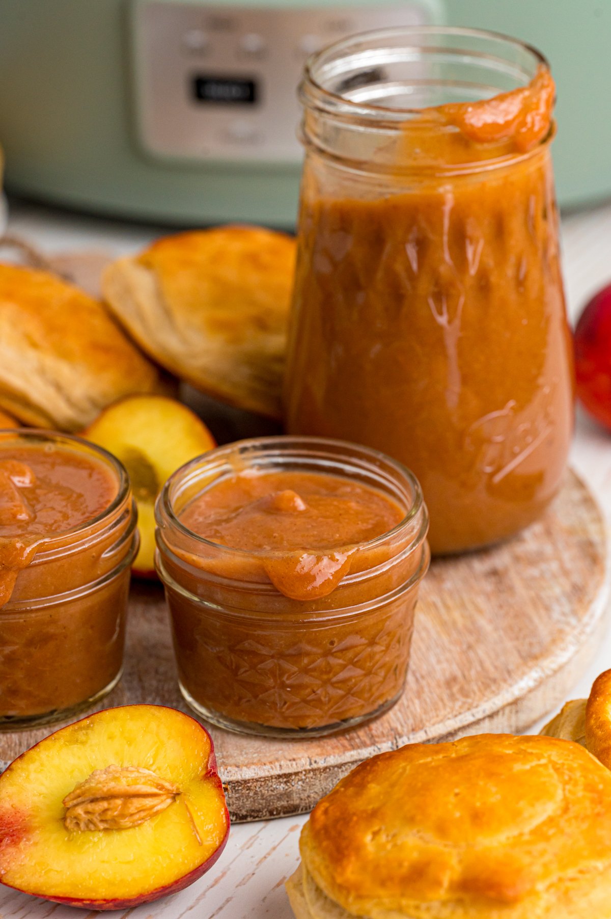 Jars of peach butter in front of a crockpot.