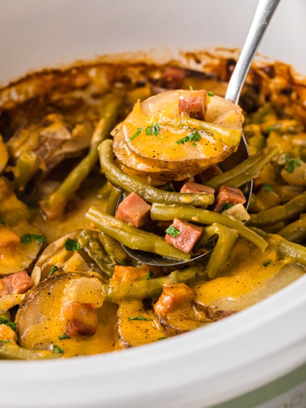 A ladle scooping out some ham, potatoes, and green beans from a slow cooker.