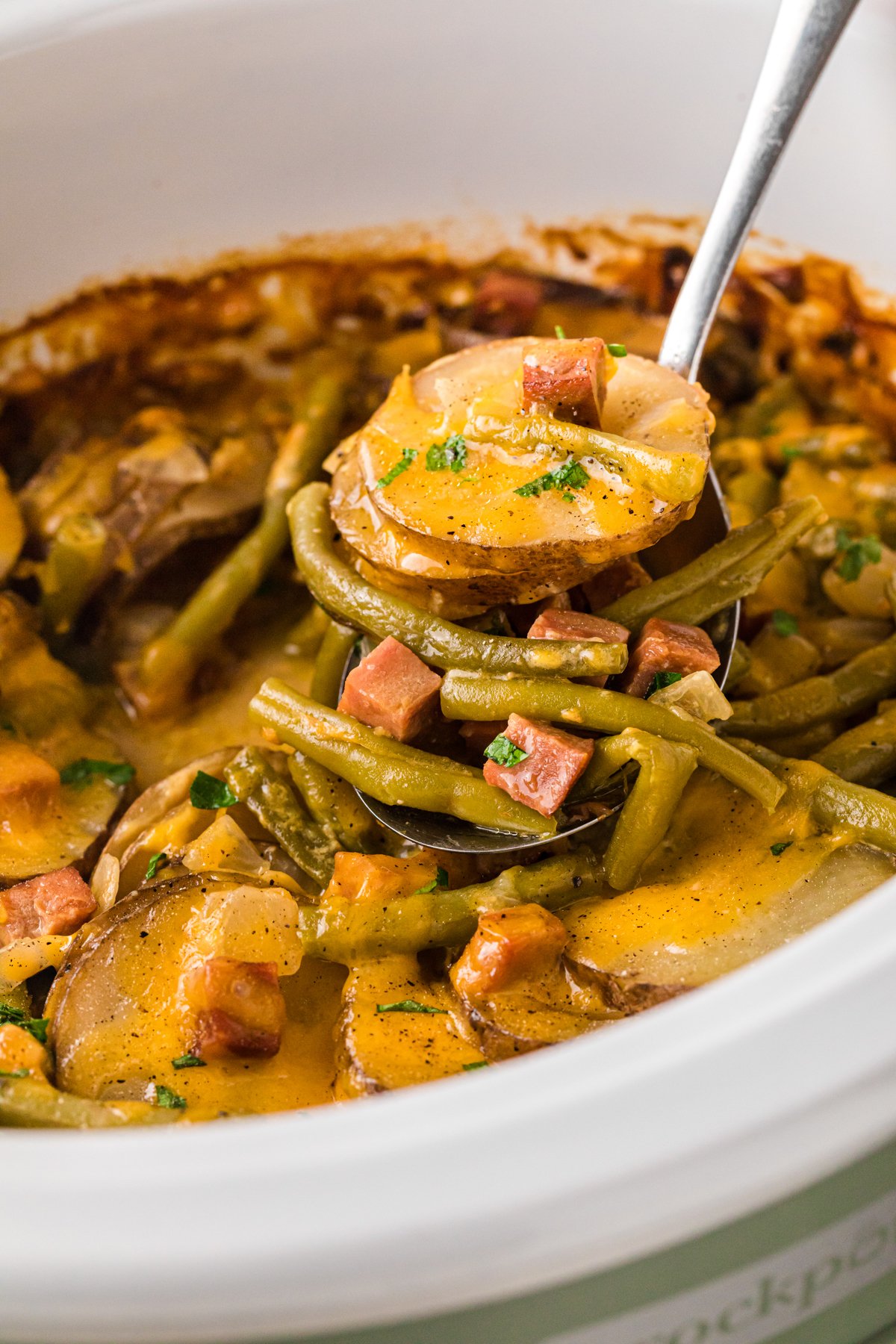 A ladle scooping out some ham, potatoes, and green beans from a slow cooker.