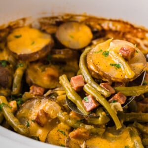 A ham dinner meal in a crockpot with a ladle scooping some out.