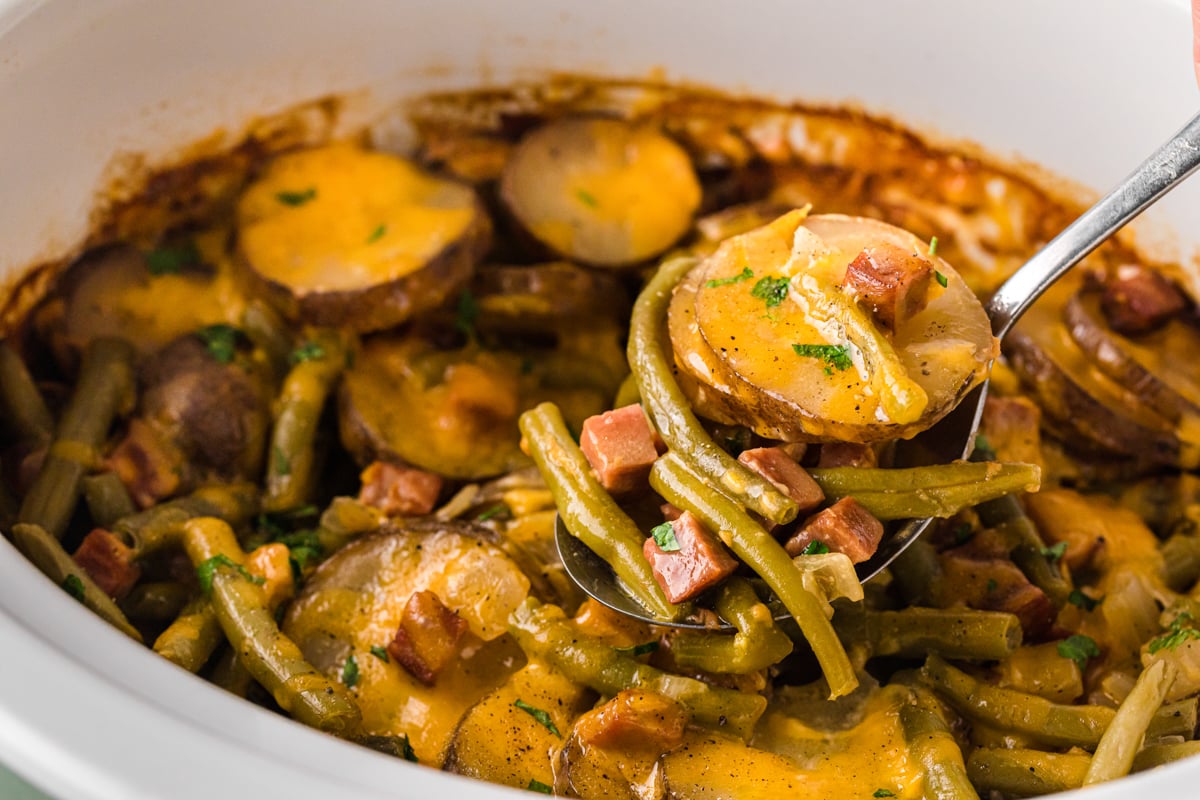 A ham dinner meal in a crockpot with a ladle scooping some out.