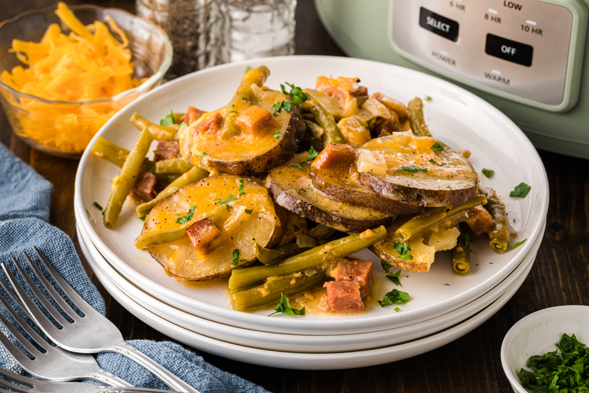 A plate of vintage ham and potato dinner in front of a slow cooker.