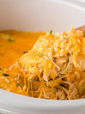 A crockpot of cheesy chicken and rice casserole with a spoon taking some out.