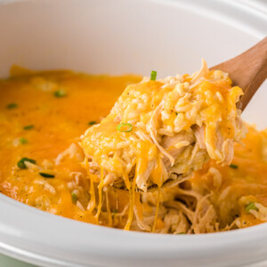 A crockpot of cheesy chicken and rice casserole with a spoon taking some out.