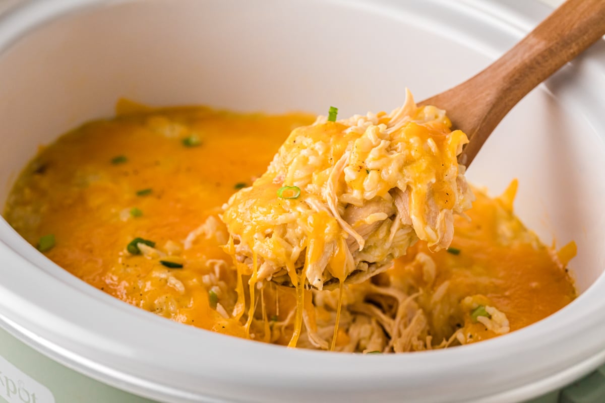 A crockpot of cheesy chicken and rice casserole with a spoon taking some out.
