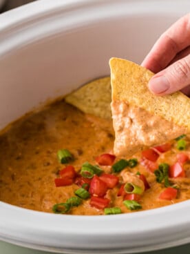 A hand holding a dip-covered tortilla chip over a crockpot of dip.