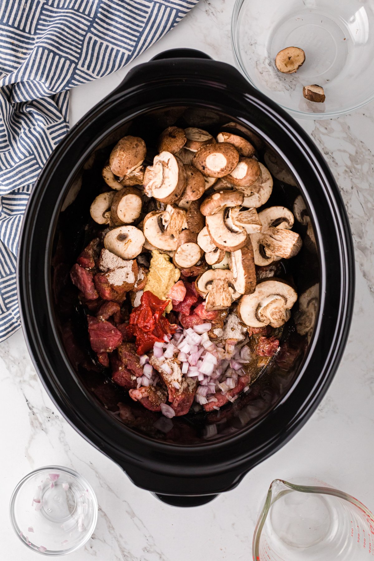 Mushrooms, shallot, and water added to beef mixture in a crockpot.