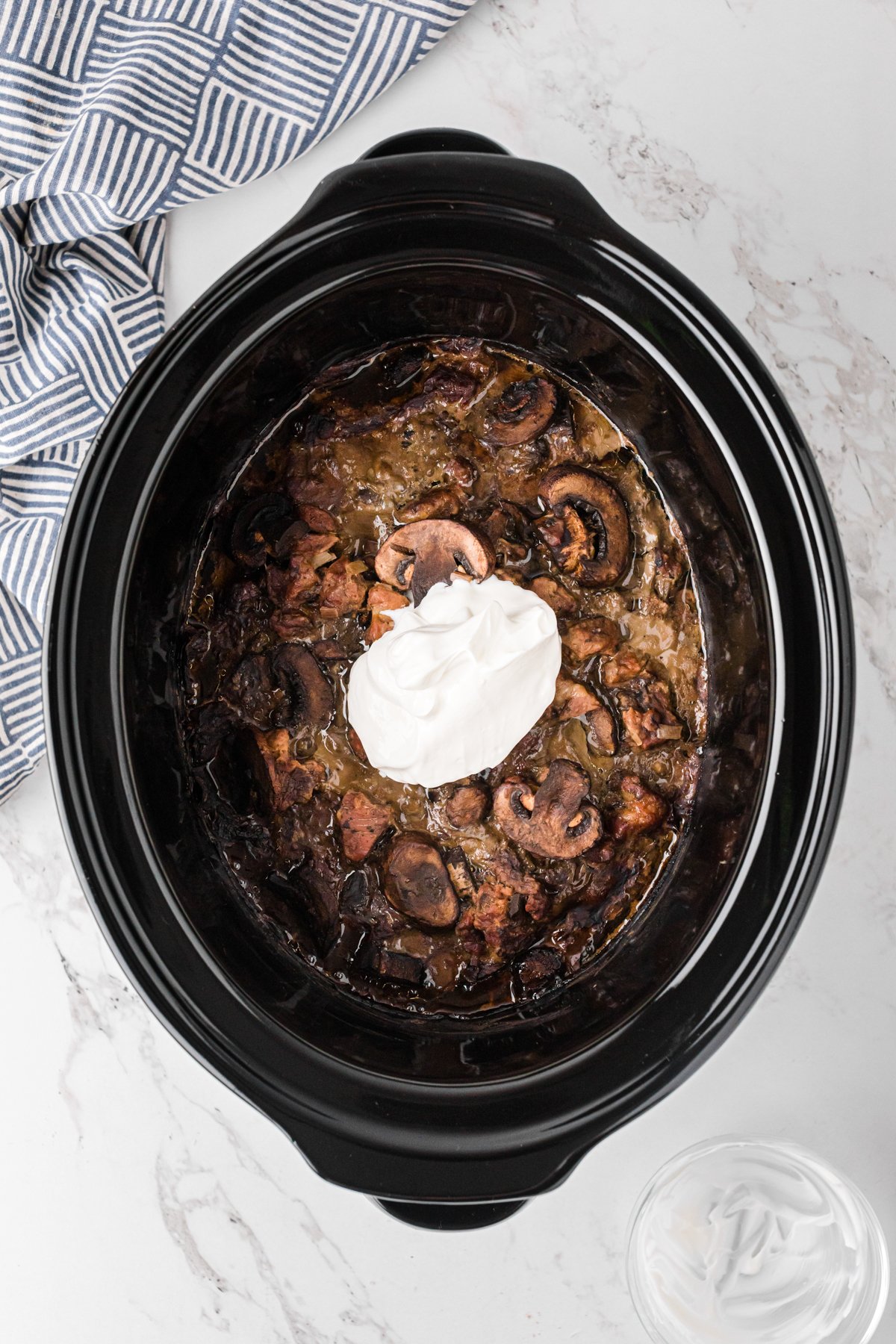 Sour cream added to cooked meat and mushroom mixture in a crockpot.
