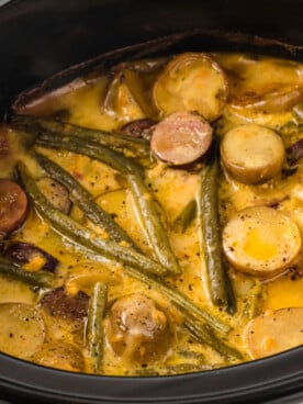 A crockpot with cooked potatoes, green beans, and kielbasa in a cheesy ranch sauce.