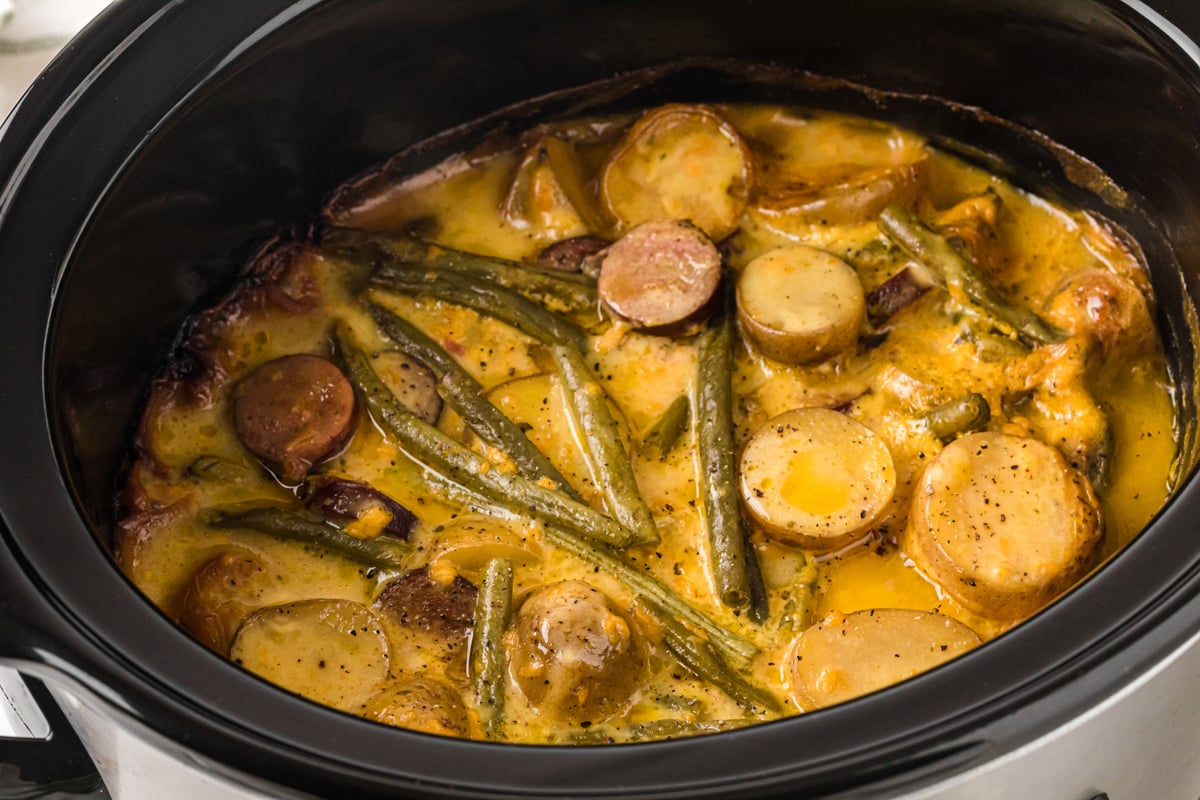 A crockpot with cooked potatoes, green beans, and kielbasa in a  cheesy ranch sauce.