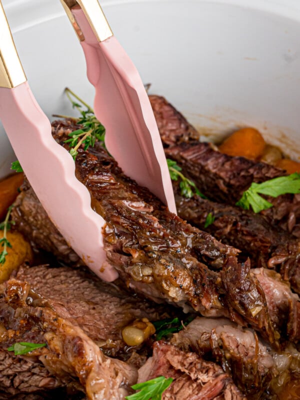 Tongs grabbing a piece of pot roast from a crockpot.