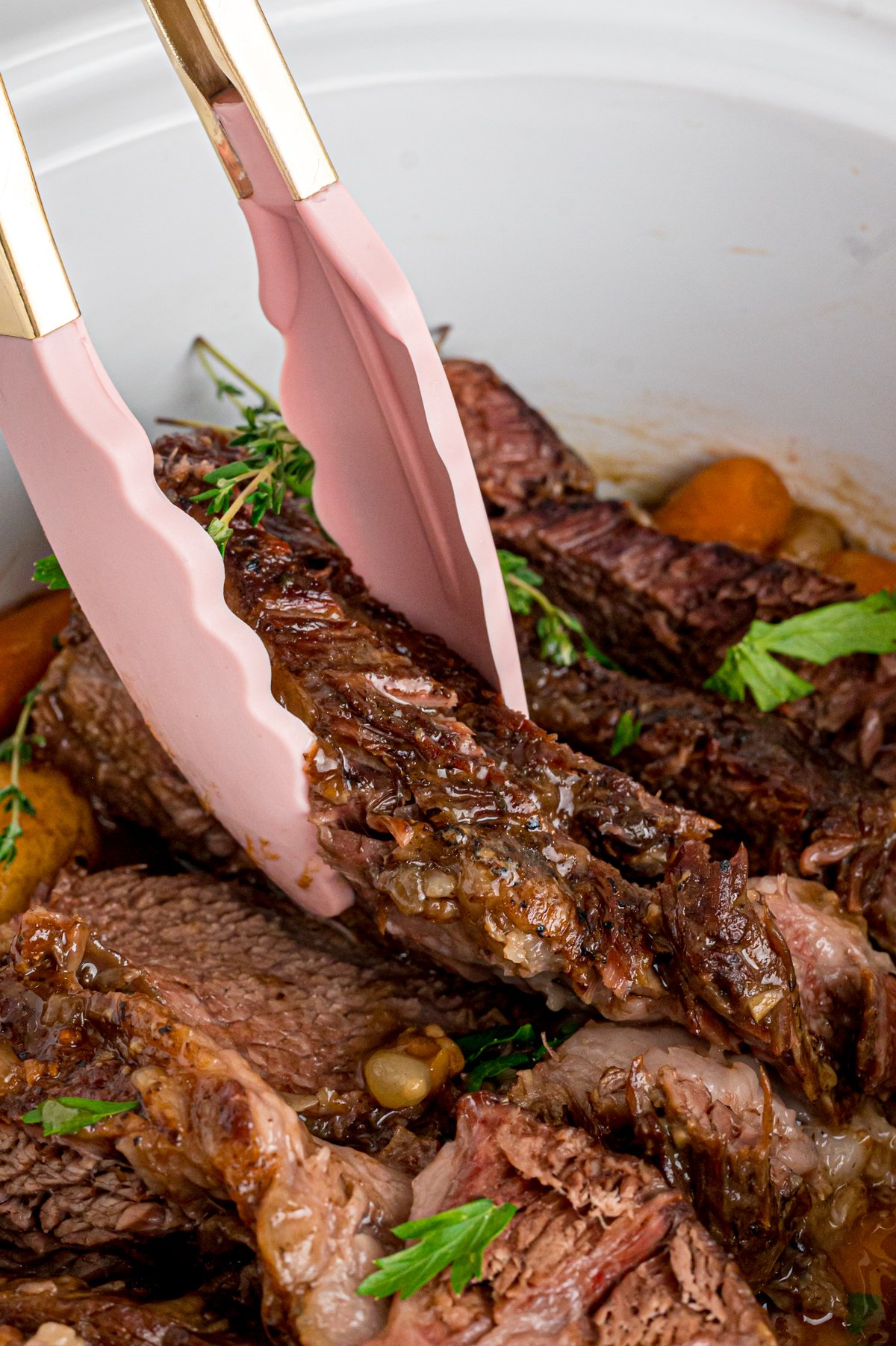 Tongs grabbing a piece of pot roast from a crockpot.