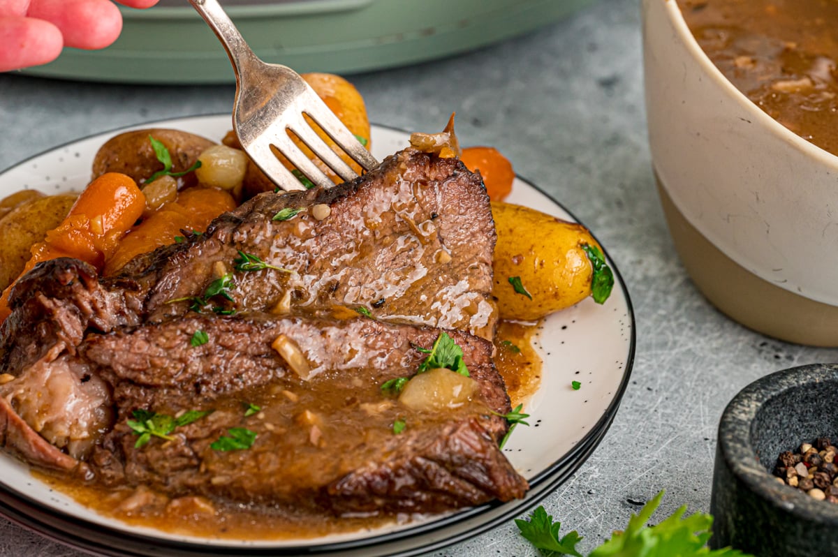 A fork grabbing a piece of meat from a plate.