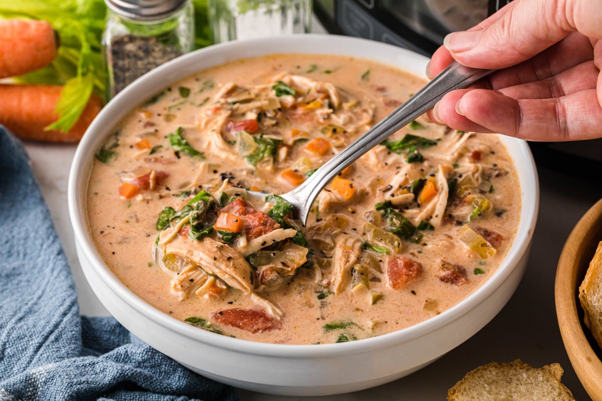 A hand grabbing a spoonful of soup from a bowl.
